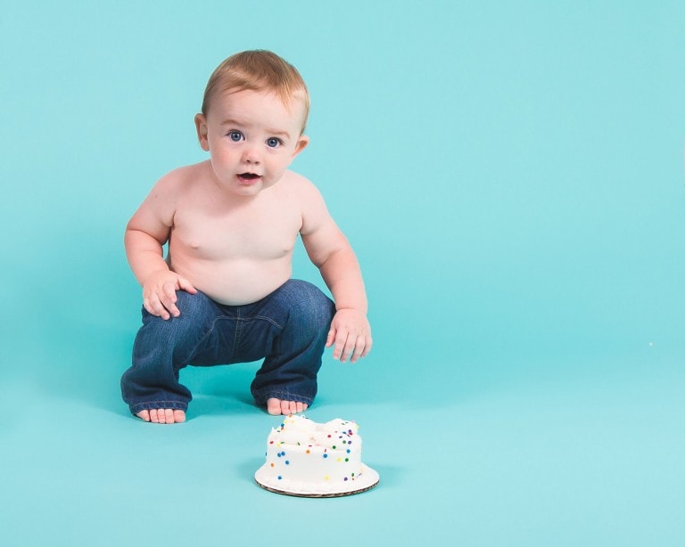 Baby boy in blue jeans at cake smash session with a white cake with sprinkles