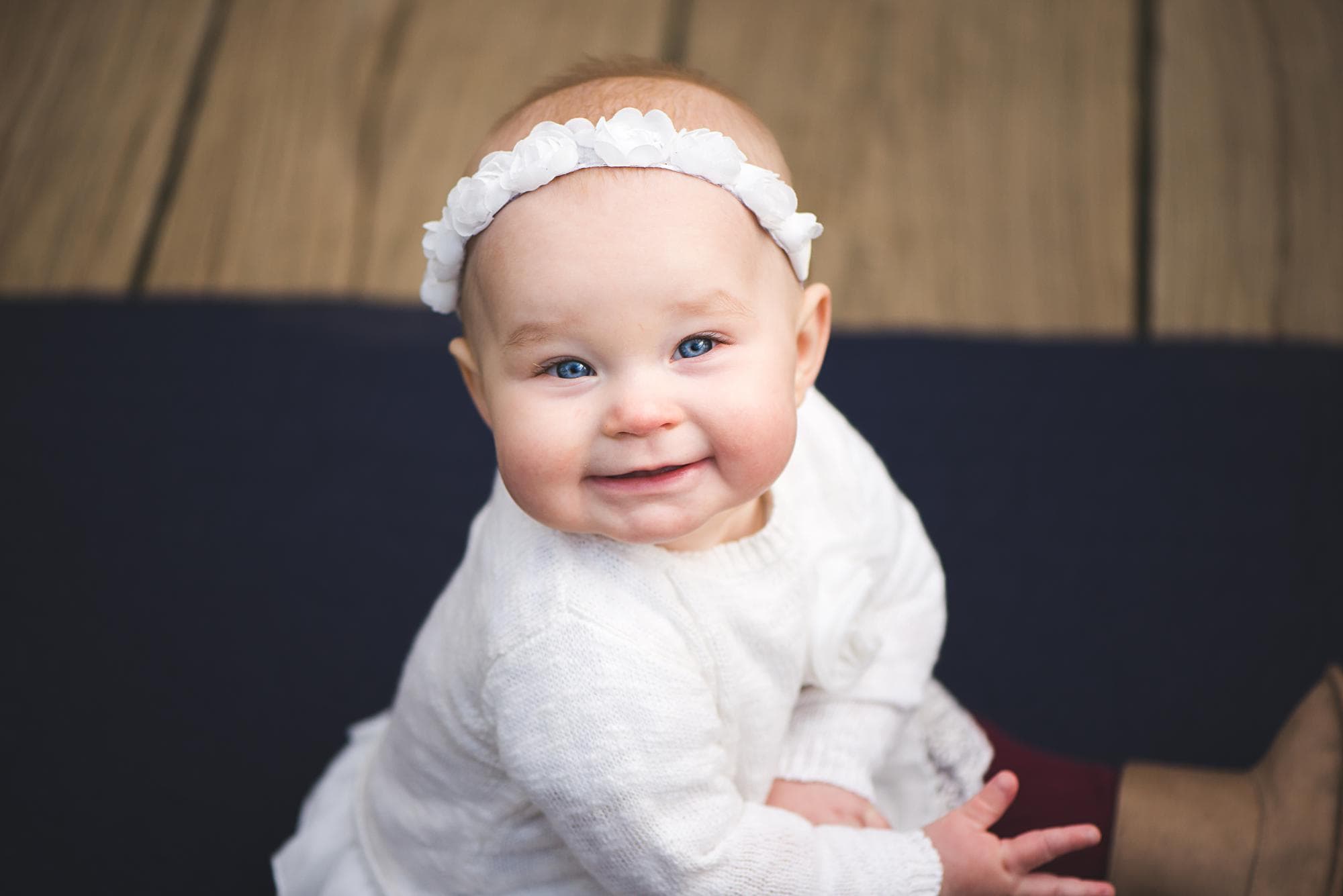 Infant girl with white dress and headband looking up at camera