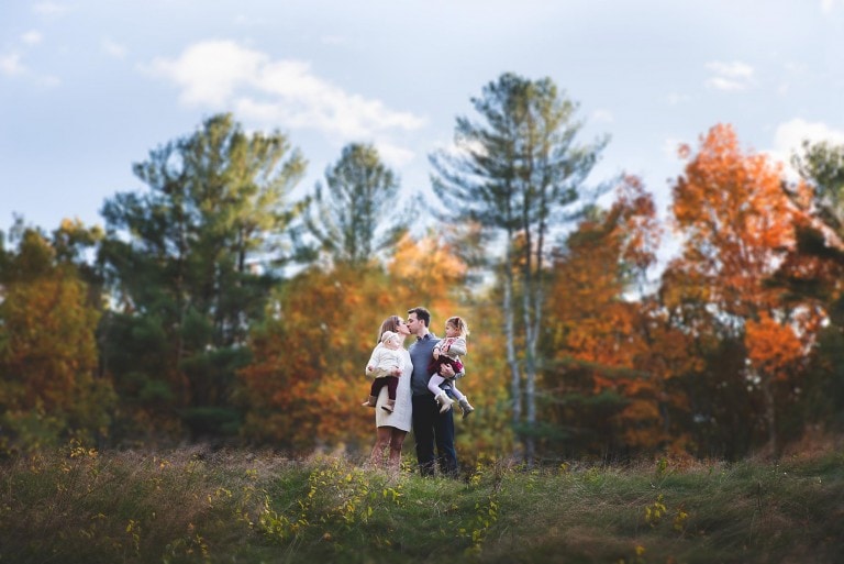 Family of 4 with mom and dad kissing outside with Fall colors