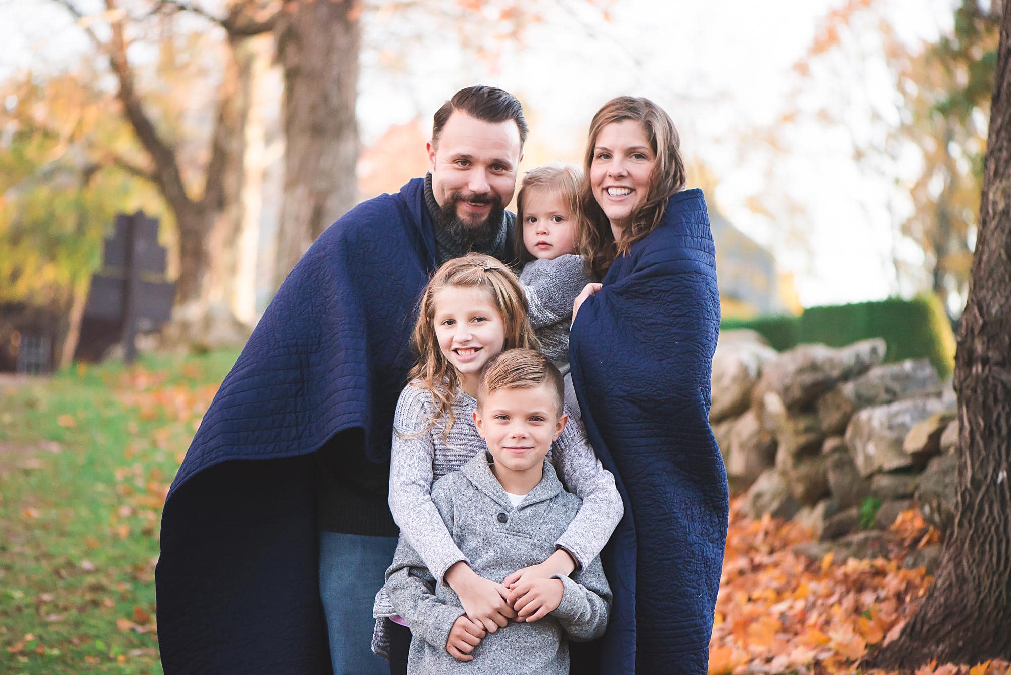 Family of 5 snuggling in blue blanket under Fall trees