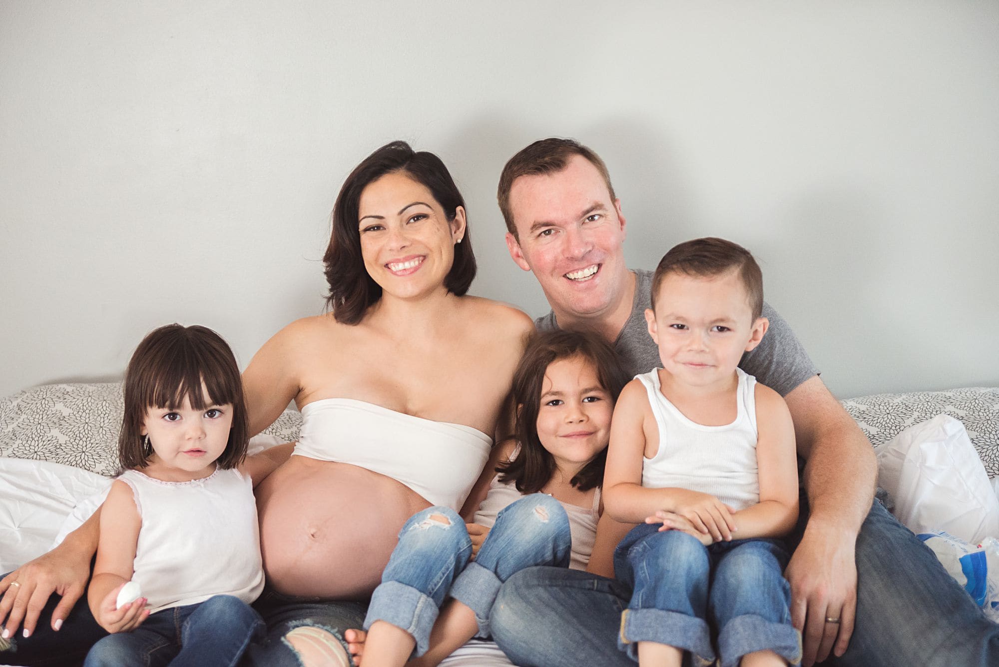 Studio style family maternity portrait with three children wearing denim and white