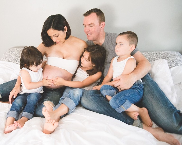Family maternity photo with three children, everyone dressed in blue jeans with white and grey tops