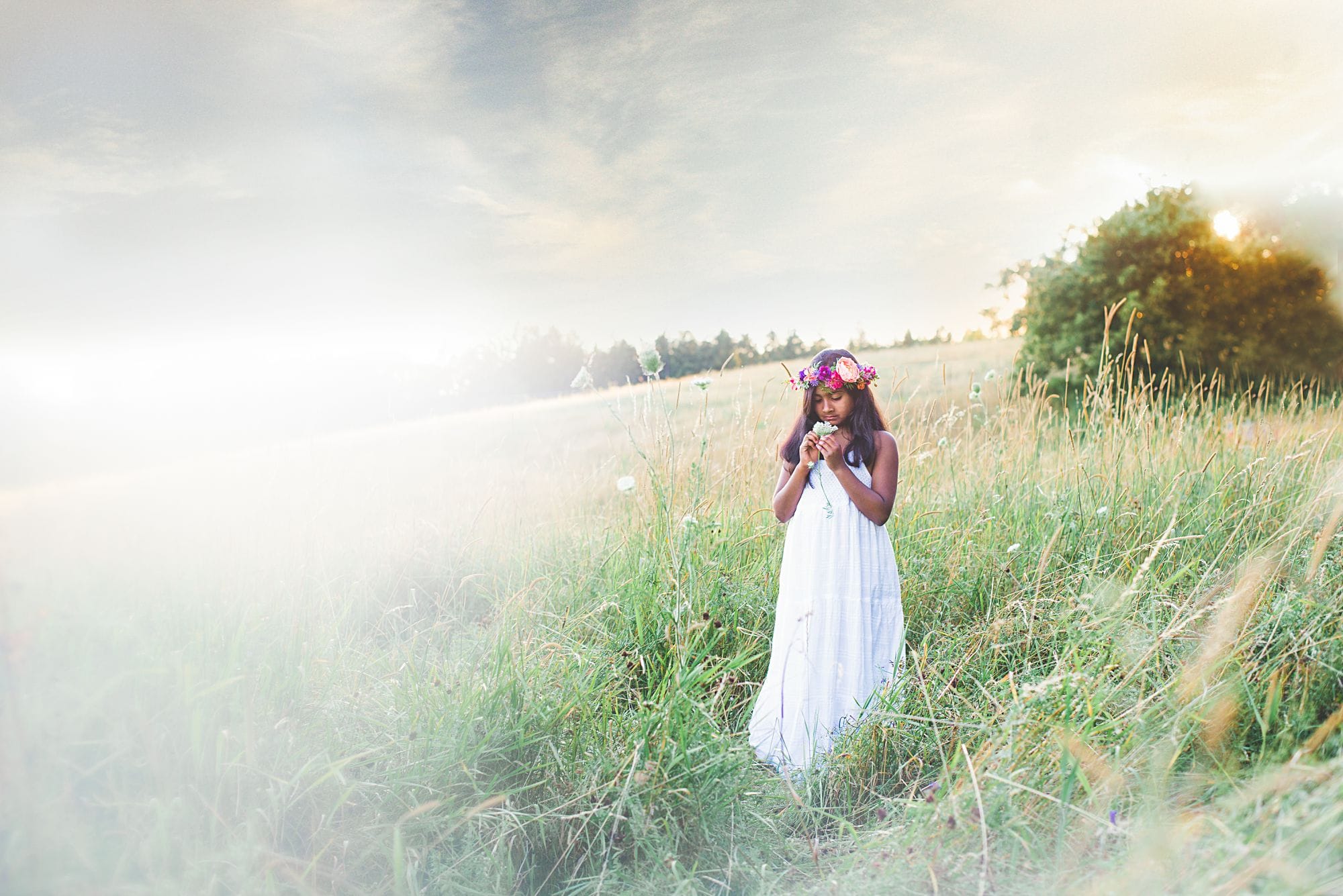 Young girl in an open field wearing a long white dress wearing flowers in her hair