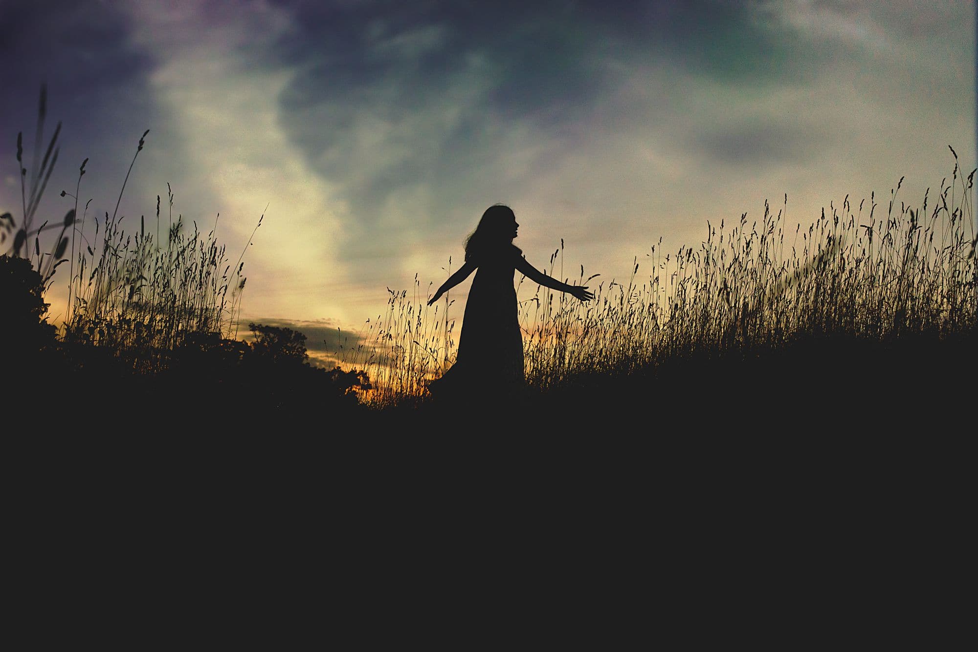 Silhouette horizon at sunset with young girl dancing and twirling