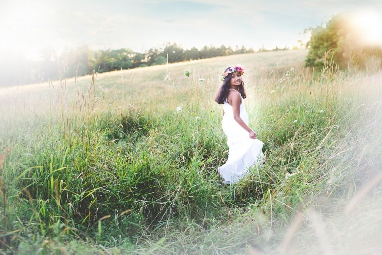 Tween girl twirling in a grassy field wearing a white dress and pink floral crown