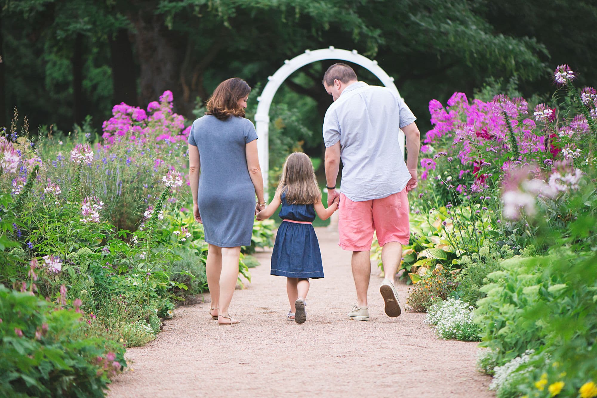 Family walking away through a garden with pink flowers, wearing blue dresses and salmon shorts